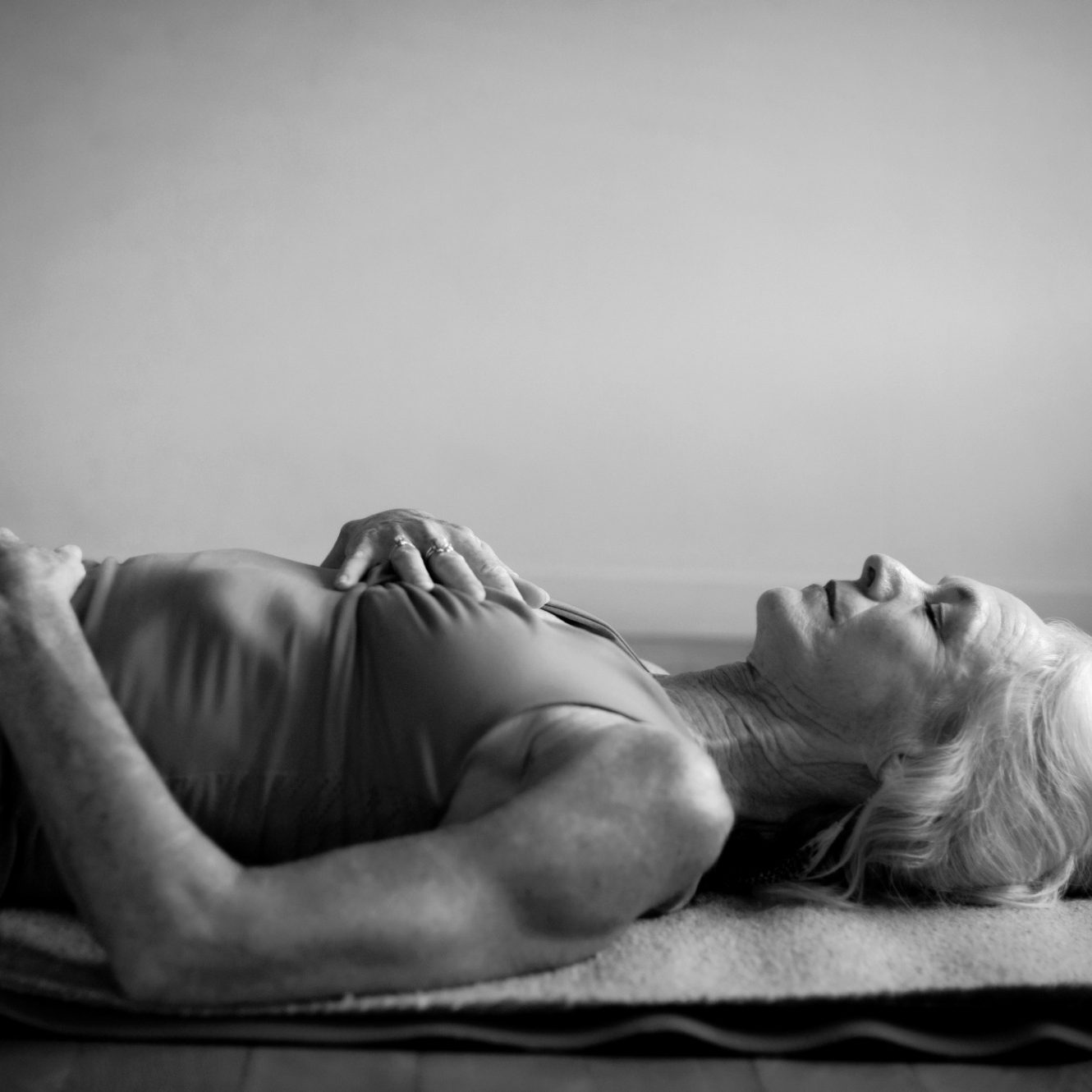 A woman lies on a yoga mat, eyes closed, in a relaxed position.