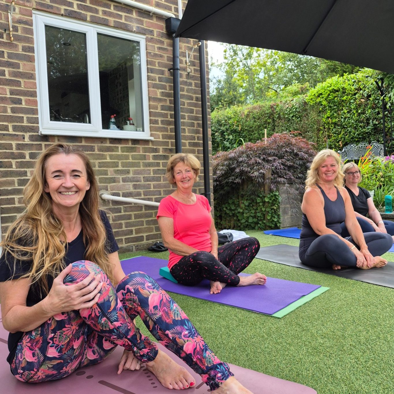 Summer yoga at home Four women sitting on yoga mats outside, smiling and engaging in a yoga session.