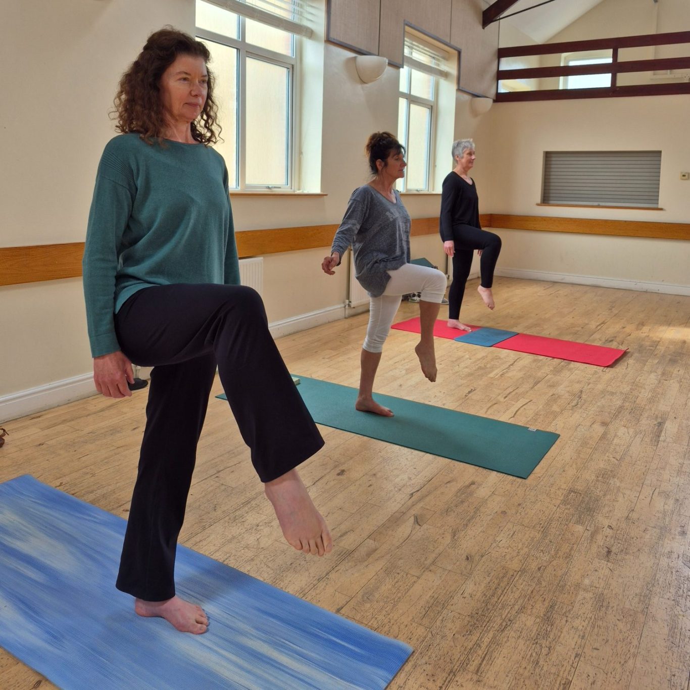 yoga balance at crowborough Three people practicing yoga poses on colourful mats in a bright, spacious studio.