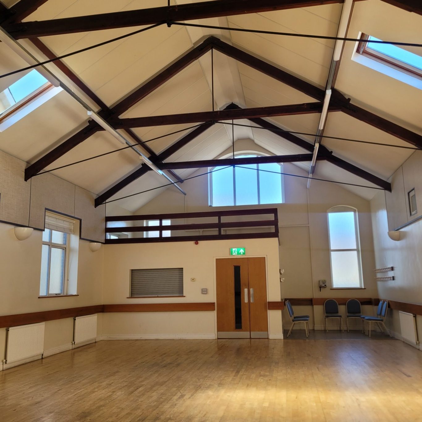 Spacious hall with wooden floor, high ceiling, and large windows for natural light.